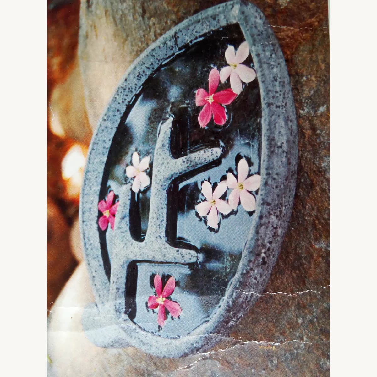 Oval stone water bowl with a carved geometric divider and floating flowers