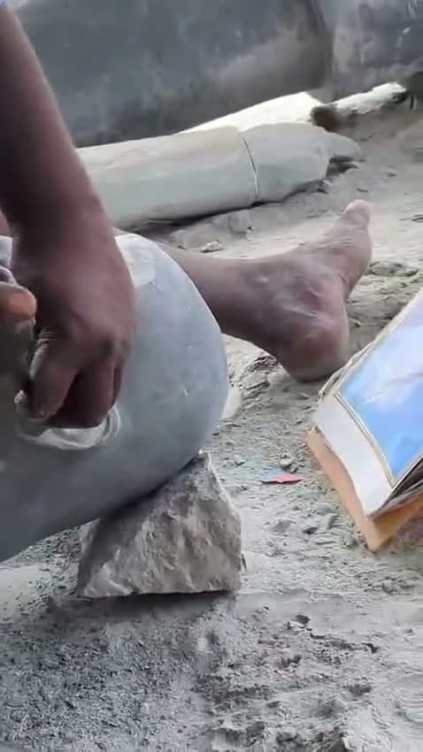 An artisan's hands working on the ear of a stone portrait with a chisel